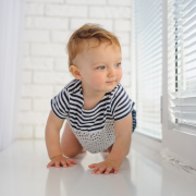 Little cute baby crawls on the floor looking at window blinds