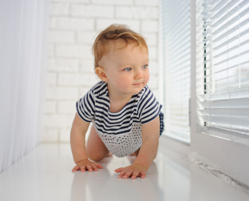Little cute baby crawls on the floor looking at window blinds