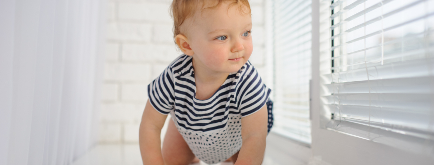 Little cute baby crawls on the floor looking at window blinds