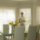 Woman holding glass of water standing behind the kitchen table appreciating the light control done by Timberstyle venetian blinds